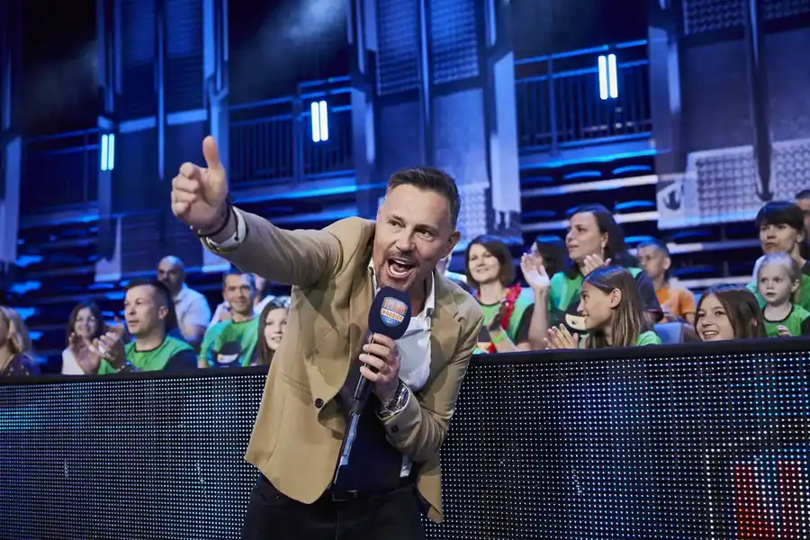 Prowadzący z mikrofonem Ninja Warrior na tle rozentuzjazmowanej publiczności — dzieci z Ninja Club Kraków